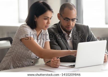 Female asian mentor teaching african male trainee intern looking at laptop, manager consulting client pointing at computer, teacher supervisor explaining online work to coworker sit at office desk Royalty-Free Stock Photo #1410209846