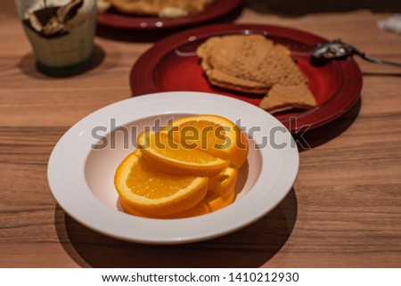 Creative and healthy diet food concept for slice oranges on white and round plate, placed near a brown and yummy waffle plate on a wooden table. Image taken from a cafe during dinner time.