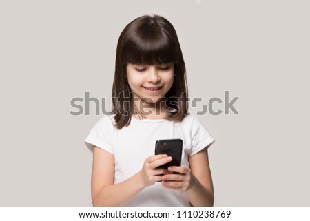 Six years old girl hold smart phone enjoy online communication with friend, play new free game use application isolated on grey beige background, parental control, gen z, modern wireless tech concept