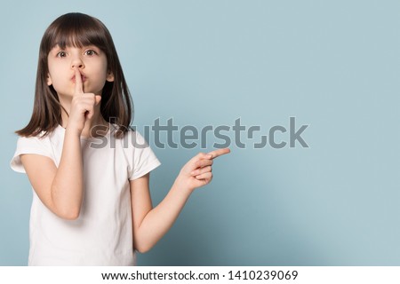 Adorable six years old little girl holding finger on lips symbol of hush gesture of asking to be quiet. Silence or secret concept image isolated on blue studio background with copy free space for text Royalty-Free Stock Photo #1410239069