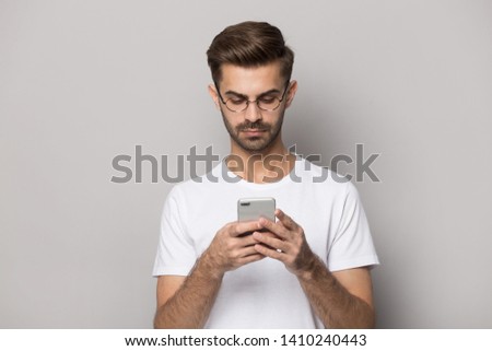 Young man wearing glasses white t-shirt isolated on beige studio background use cellular freelancer work in internet check e-mail texting message, social network user holding gadget read media concept