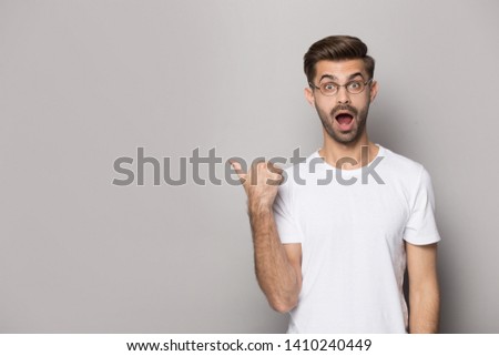 Amazed funny guy wearing white t-shirt glasses point finger aside at copy space advertise better offer huge discount opportunity, eye vision correction procedure, good services, isolated on beige wall