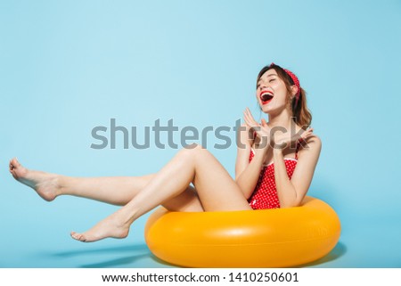 Image of a beautiful young pin up pretty summer girl in swimwear posing isolated over blue background in inflatable ring.