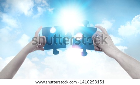 Two hands holding a puzzle pieces agains of blue sky background and sun. Business, support, finding the right decision concept. 