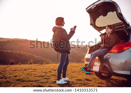 Mother and daughter camping outdoor and taking selfie with smart phone while sitting in open car trunk