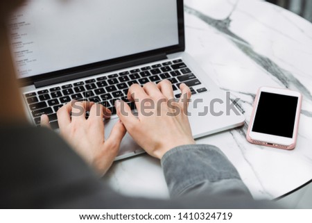 Close up of a woman working on a blank screen laptop computer over table indoors with blank screen mobile phone