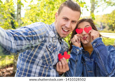 Happy young couple with paper hearts taking selfie outdoors