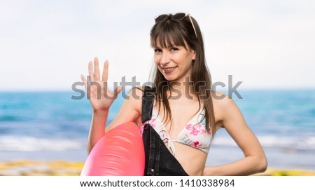 Young woman in bikini counting five with fingers at the beach