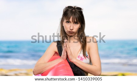 Young woman in bikini keeps palm together. Person asks for something at the beach