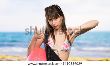 Young woman in bikini making good-bad sign. Undecided between yes or not at the beach