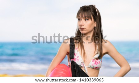 Young woman in bikini making doubts gesture looking side at the beach