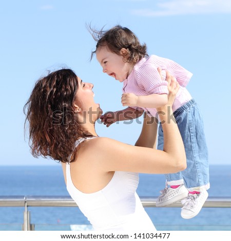Pretty mum laughing and raising her baby girl with the sea in the background