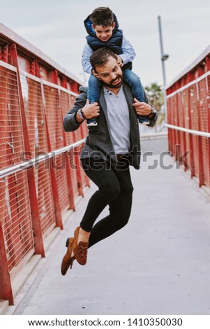 A father in a bridge with red columns jumps with his young son on top of him