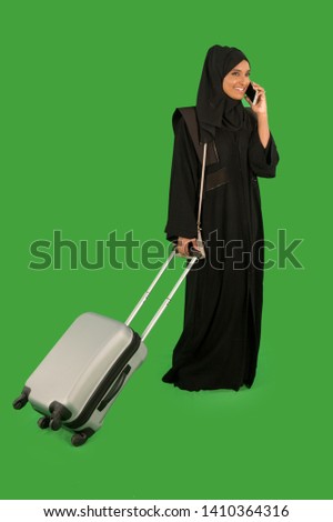 Emirati woman talking on mobile phone while carrying a suitcase