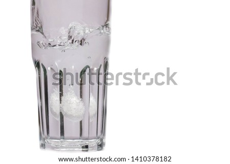 Effervescent tablet falling into a glass cup with pure water isolated on a white background. Medical preparation in the form of a bubble-letting pill. The process of dissolving the drug in water.