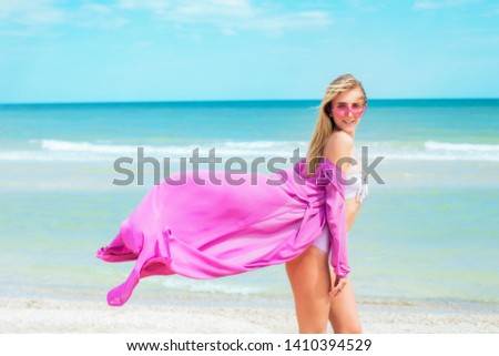 A beautiful young girl with long hair in a pink swimsuit  relax on beach in the sea in sunny hot day