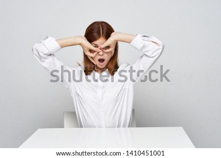 A woman holds joined fingers in front of her eyes and opened her mouth in a bright isolated room              