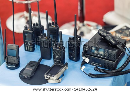 Many portable radio transceivers on table at technology exhibition. Different walkie-talkie radio set. Communication devices choice for military and civil use Royalty-Free Stock Photo #1410452624