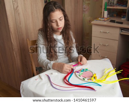 Teenager girl decorate with stripes of paper, quilling .Hands child while creative work making decorations paper.