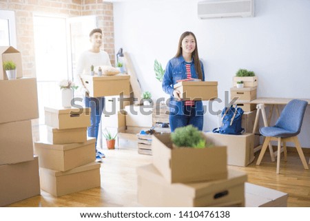 Beautiful young asian couple looking happy holding cardboard boxes, smiling excited moving to a new home