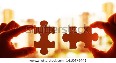 two hands trying to connect couple puzzle piece on house background. Jigsaw  wooden puzzle against home with windows.  part of whole. symbol of association and connection. business strategy