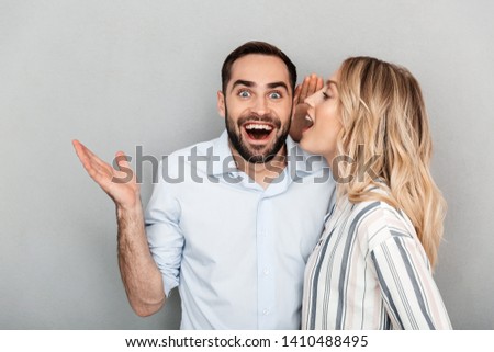 Photo of blonde woman in casual clothing screaming in ear of excited man isolated over gray background