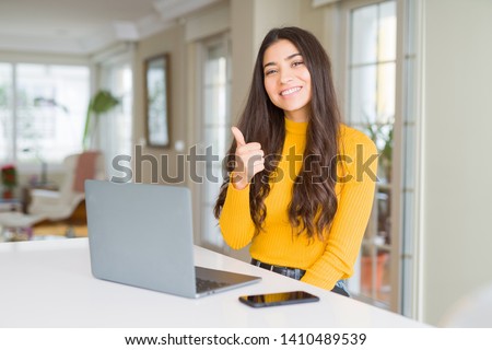 Young woman using computer laptop doing happy thumbs up gesture with hand. Approving expression looking at the camera with showing success. Royalty-Free Stock Photo #1410489539