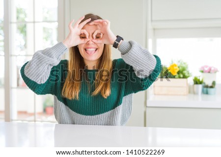Young beautiful plus size woman wearing casual striped sweater doing ok gesture like binoculars sticking tongue out, eyes looking through fingers. Crazy expression.