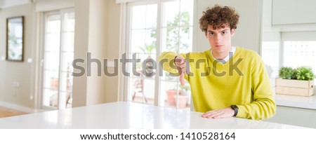 Wide angle shot of young handsome man at home looking unhappy and angry showing rejection and negative with thumbs down gesture. Bad expression.