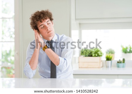 Young business man wearing a tie sleeping tired dreaming and posing with hands together while smiling with closed eyes.