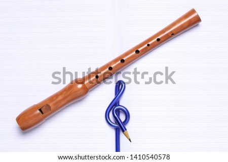 music school concept: music sol key shaped pencil  and wooden sweet flute rest on an empty music score with copy space for your text