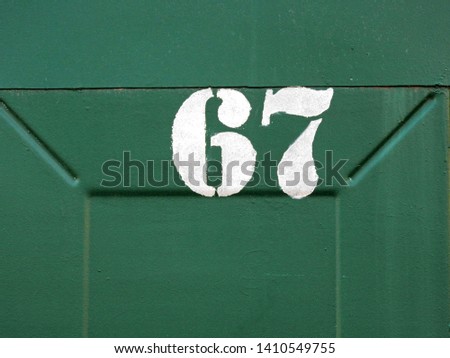 
The number is sixty seven. White numerals created with a stencil on green metal.					