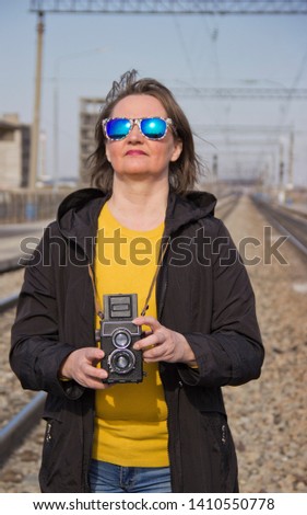Girl with an old camera at the railway station. A beautiful girl shoots on an old vintage film camera with two lenses. girl in glamorous sunglasses.