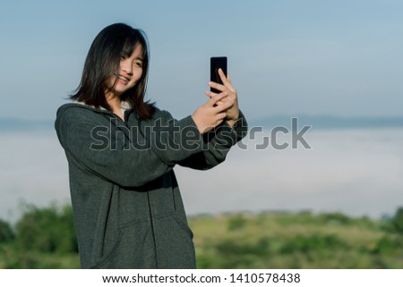 Asian woman Wearing a winter jacket, take a selfie phone, take pictures in the tourist area behind the fog and mountains with a smiling face.