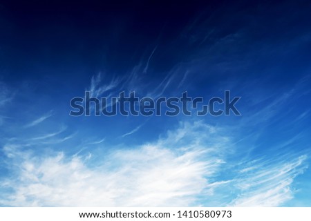 Abstract nature dark background of  white cirrus clouds expanding by wind to cover deep navy blue sky in tropical summer sunlight for backdrop or wallpaper, copy space                                  Royalty-Free Stock Photo #1410580973