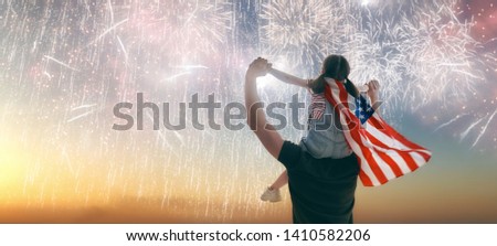 Patriotic holiday. Child sitting on shoulders of her father and  holding the Flag of the USA. America celebrate 4th of July.