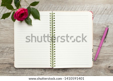 Beautiful little dark pink rose and copybook with pen on a wooden background. 
Subject photo from above