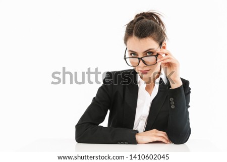 Photo of pleased female worker businesswoman dressed in formal wear looking aside while working and sitting at desk in office isolated over white background
