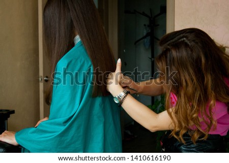 Hairdresser is working with her client in the salon. Female in pink shirt is cutting her client's hair to make new beautiful hair style. Indoor photography in a beauty salon with creme beige interior