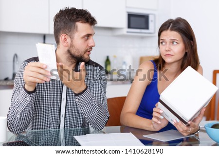 Upset young couple with financial bills and box having conflict at home