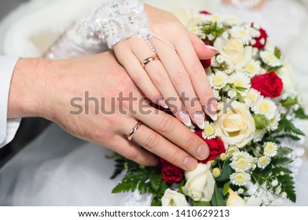 hands of the bride and groom with wedding gold rings on the background of a beautiful floral bouquet