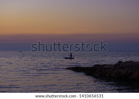 People standing on a small boat in the sea have rocks in the foreground during the time of the sun set.