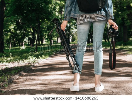 Walking woman carrying a tripod in the forest