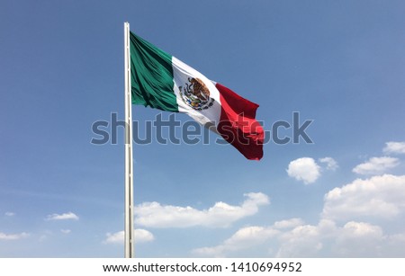 Mexican flag waving in blue sky with some clouds below