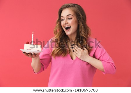Beautiful happy young girl wearing casual clothes standing isolated over pink backgound, celebrating birthday with cake