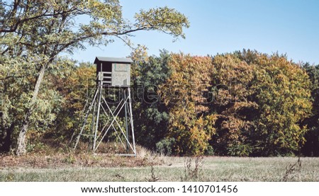Retro toned picture of a wooden deer hunting pulpit at the edge of a forest and field.
