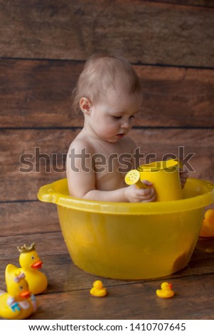 One year old baby bathed in a yellow basin and playing with rubber ducks. Soap bubbles and baby bathing. Dark wooden background. Anniversary. Girl. 