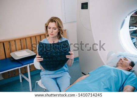 attentive radiologist examining radiology diagnosis near patient lying on mri scanner bed 