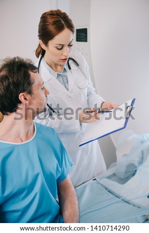cropped view of attentive doctor showing clipboard with diagnosis to patient 