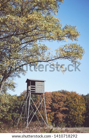 Retro toned picture of a wooden deer hunting pulpit at the edge of a forest and field.
